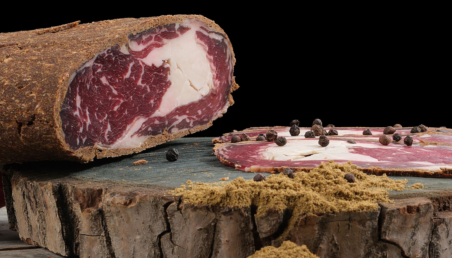 Detailed close-up of cured meat slices with ground peppercorns and spices on rustic wood.