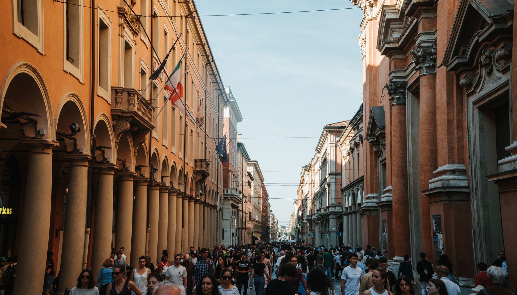 A vibrant urban scene in Bologna, Italy, showcasing historic architecture and a lively crowd.