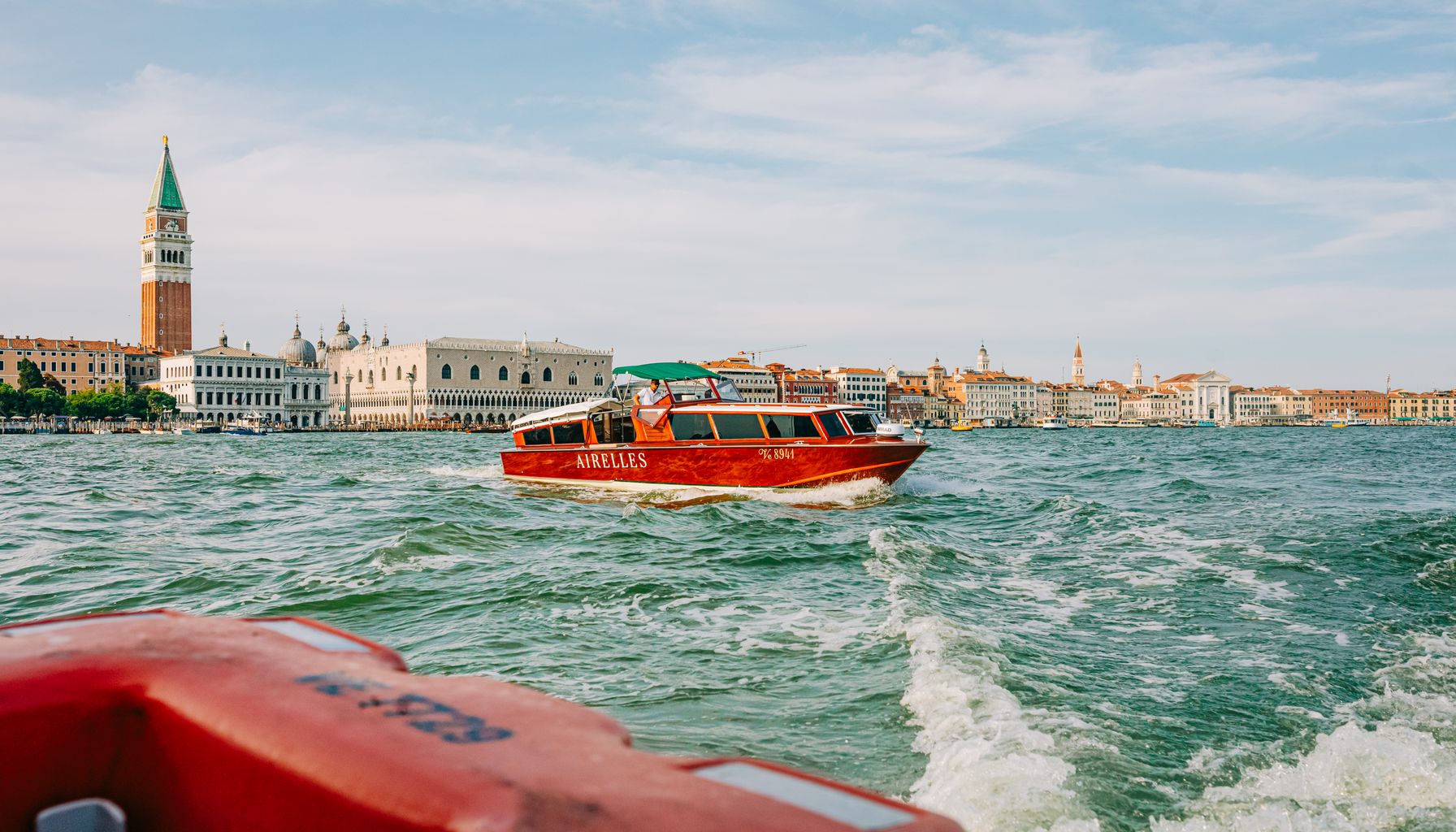 Scenic view of a water taxi cruising by the iconic San Marco Campanile in Venice during a sunny day.