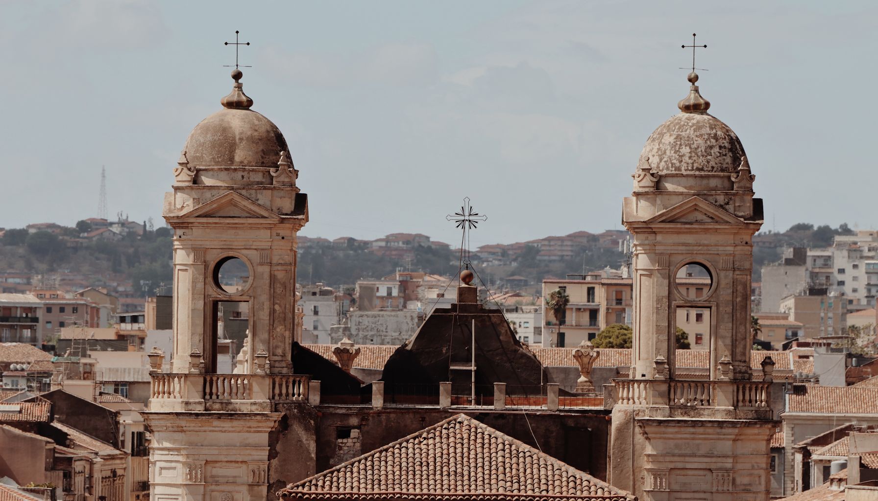 View of two classical Baroque church towers in Catania, Sicily, with cityscape background.