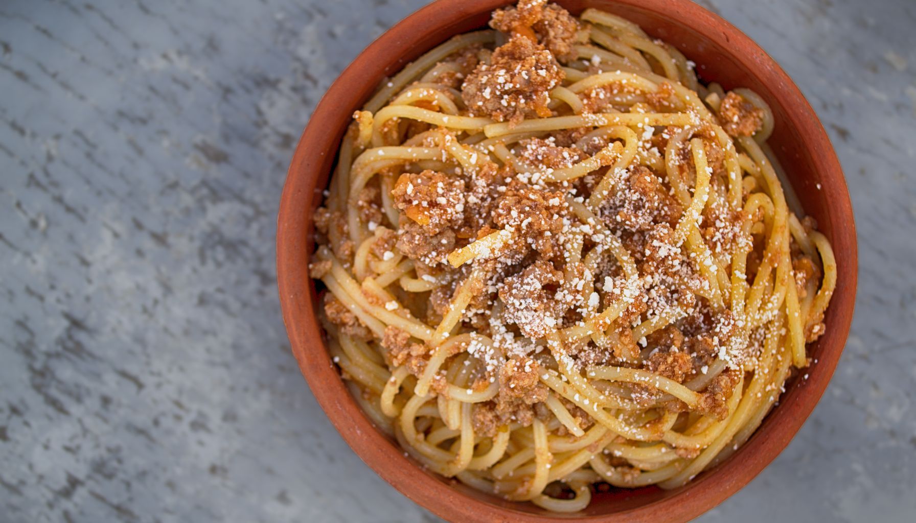 Delicious homemade spaghetti with meat sauce and parmesan served in a rustic bowl.