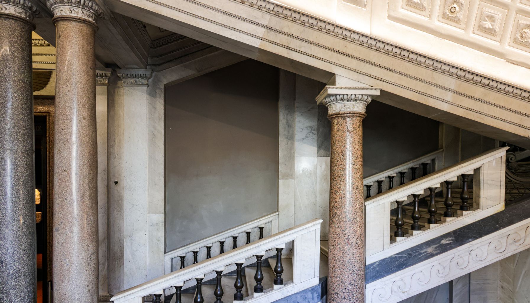 Classic Roman-style interior with ornate columns and grand staircase highlighting architectural elegance.