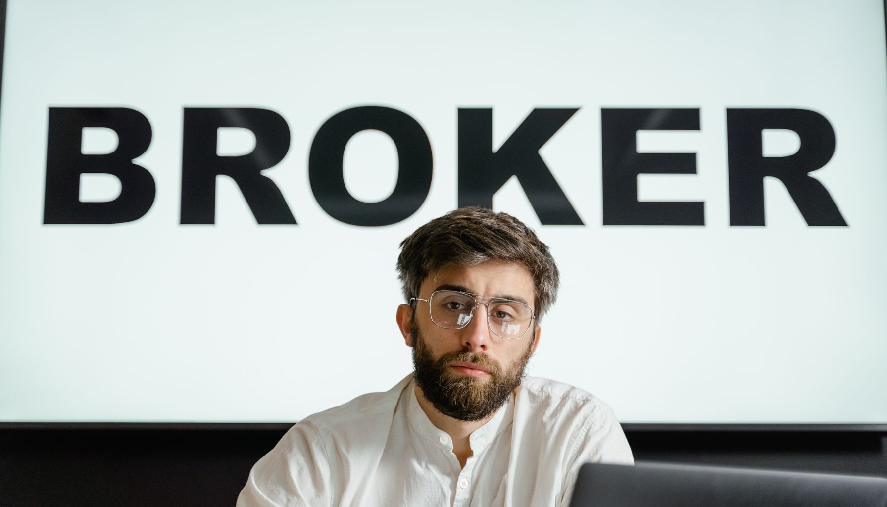 Portrait of a confident businessman sitting in an office under the sign 'BROKER'.
