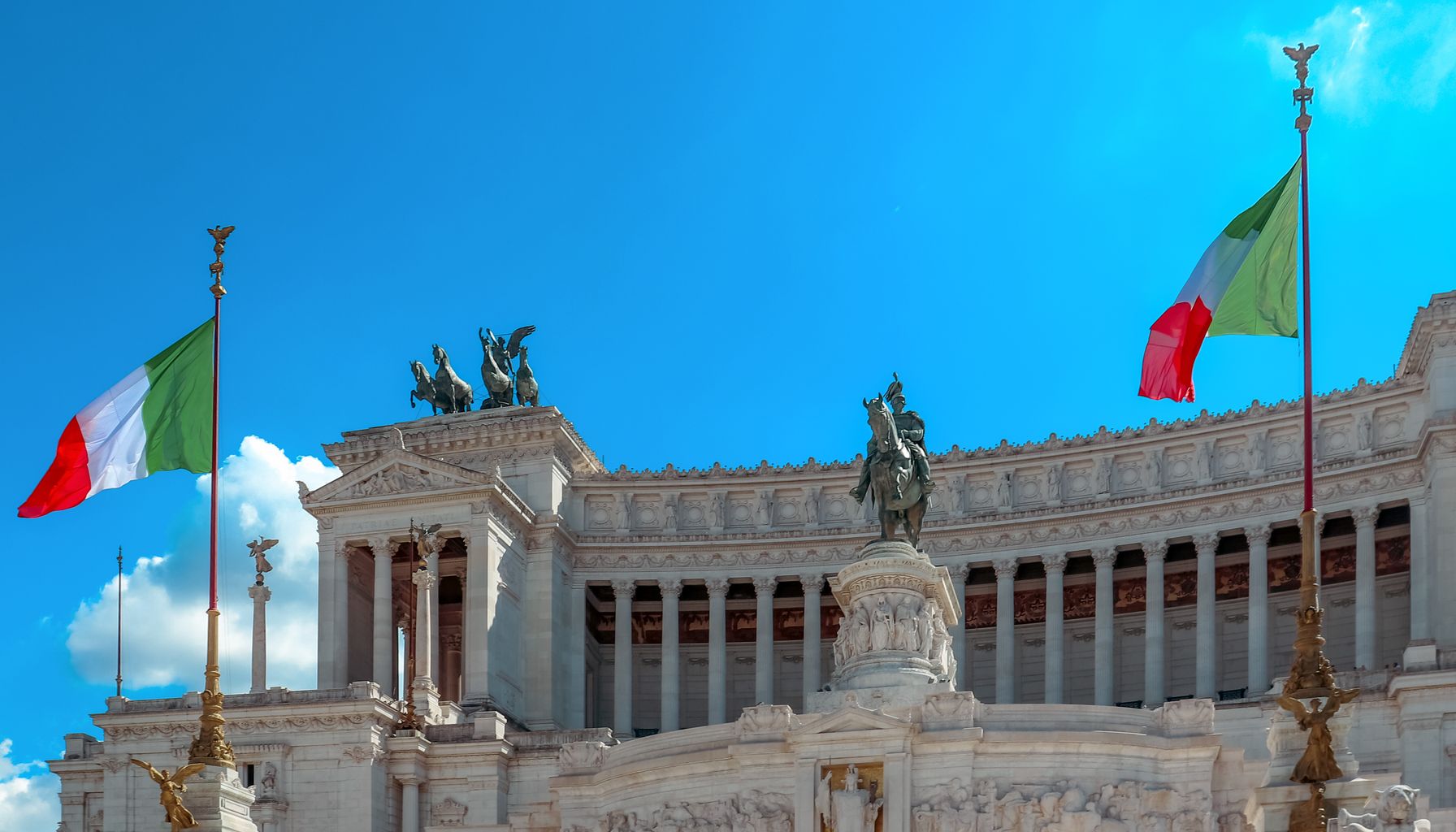 Majestic view of the Altare della Patria in Rome with Italian flags fluttering under a clear blue sky.