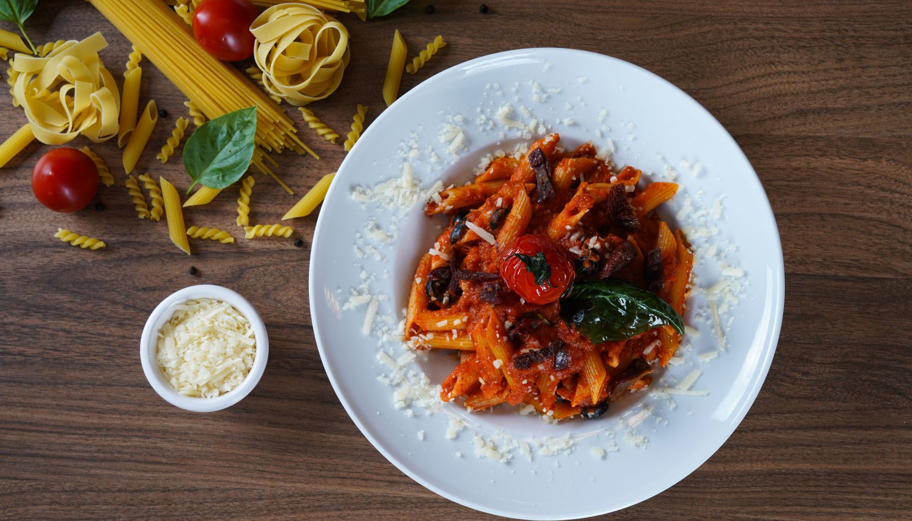 A plate of homemade pasta with a rich tomato sauce garnished with cheese, basil, and olives.