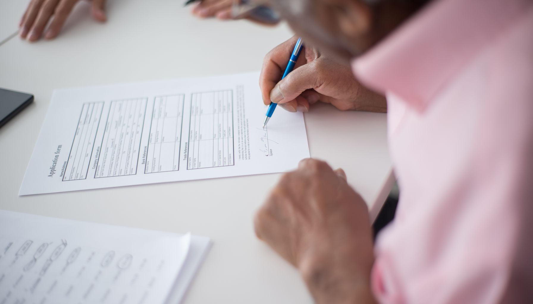 Elderly man signing important business document at desk in office setting.