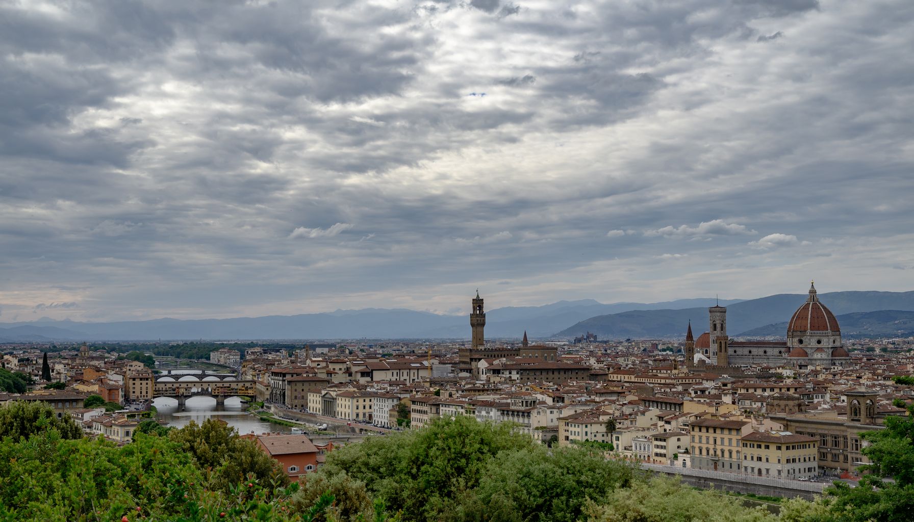 Scenic view of Florence featuring the iconic Duomo and Arno River under a dramatic sky.