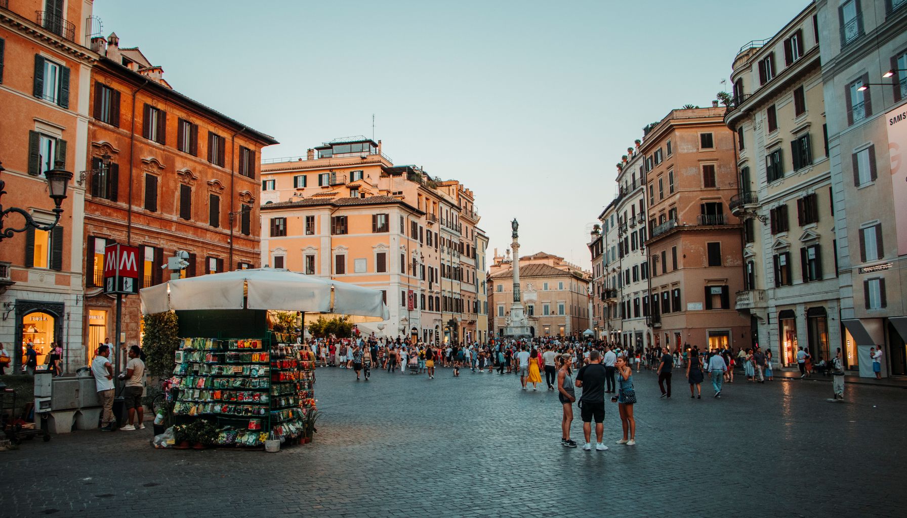 Lively urban square filled with tourists amidst historic buildings and vibrant marketplace.