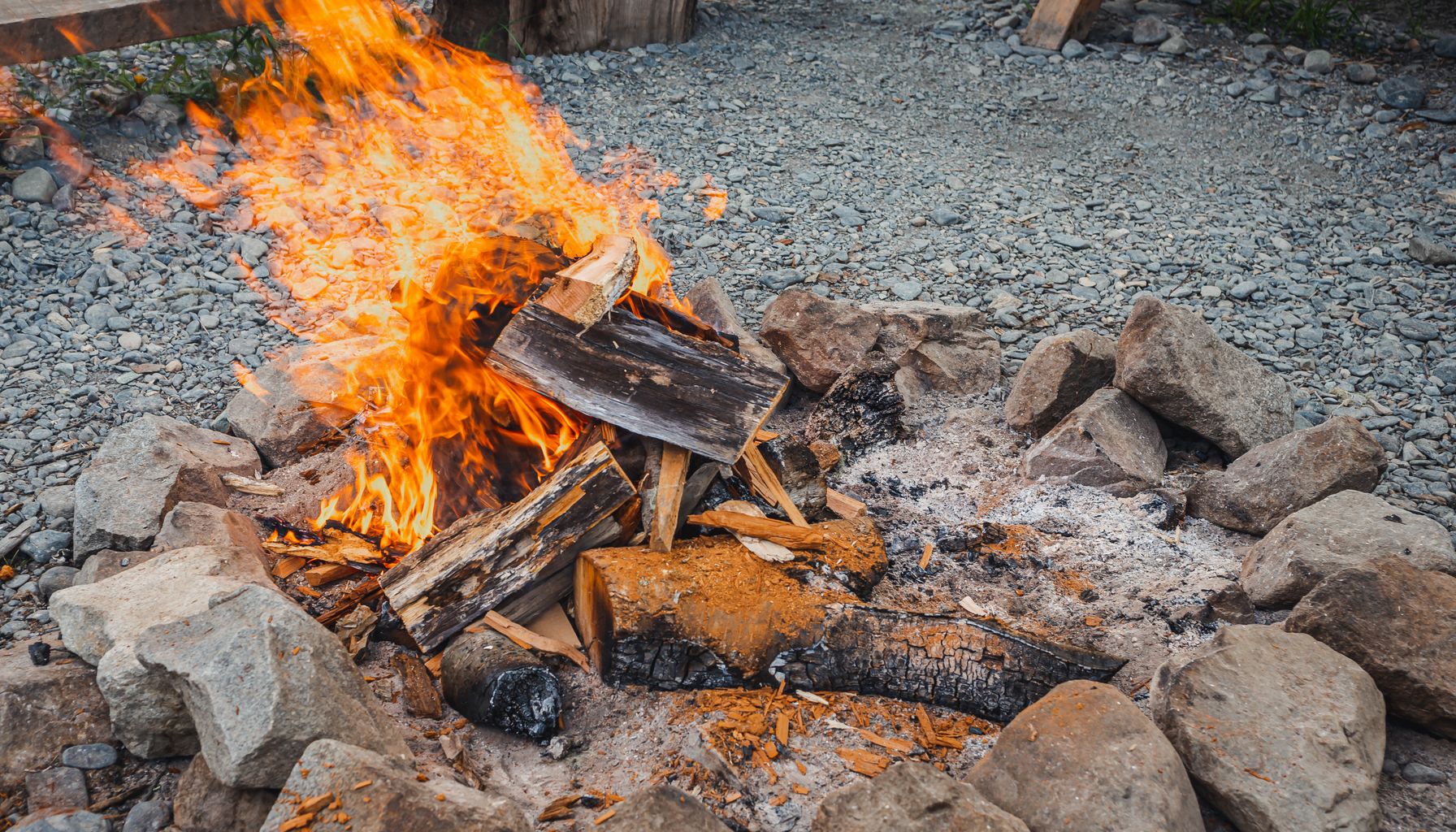 A vibrant campfire burning brightly with wood and flames, surrounded by stones in an outdoor setting.