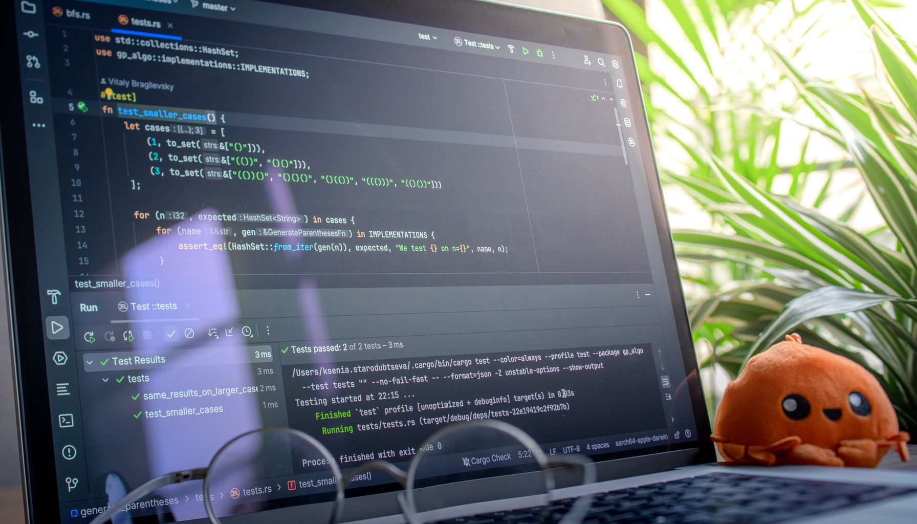 Open laptop displaying code next to a plush toy, set in a bright room with plants.