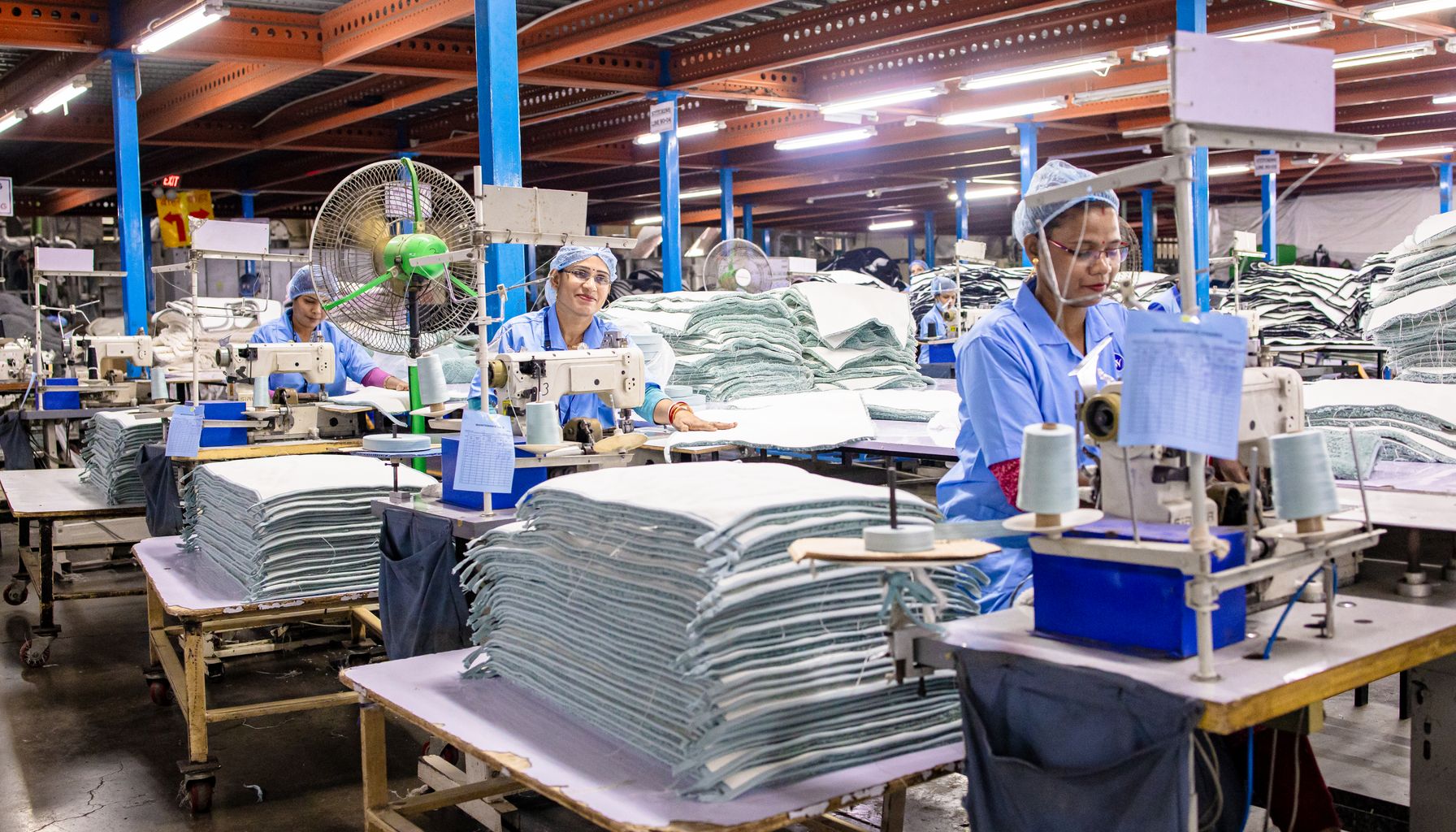 Workers in a textile factory operating sewing machines and organizing fabric.