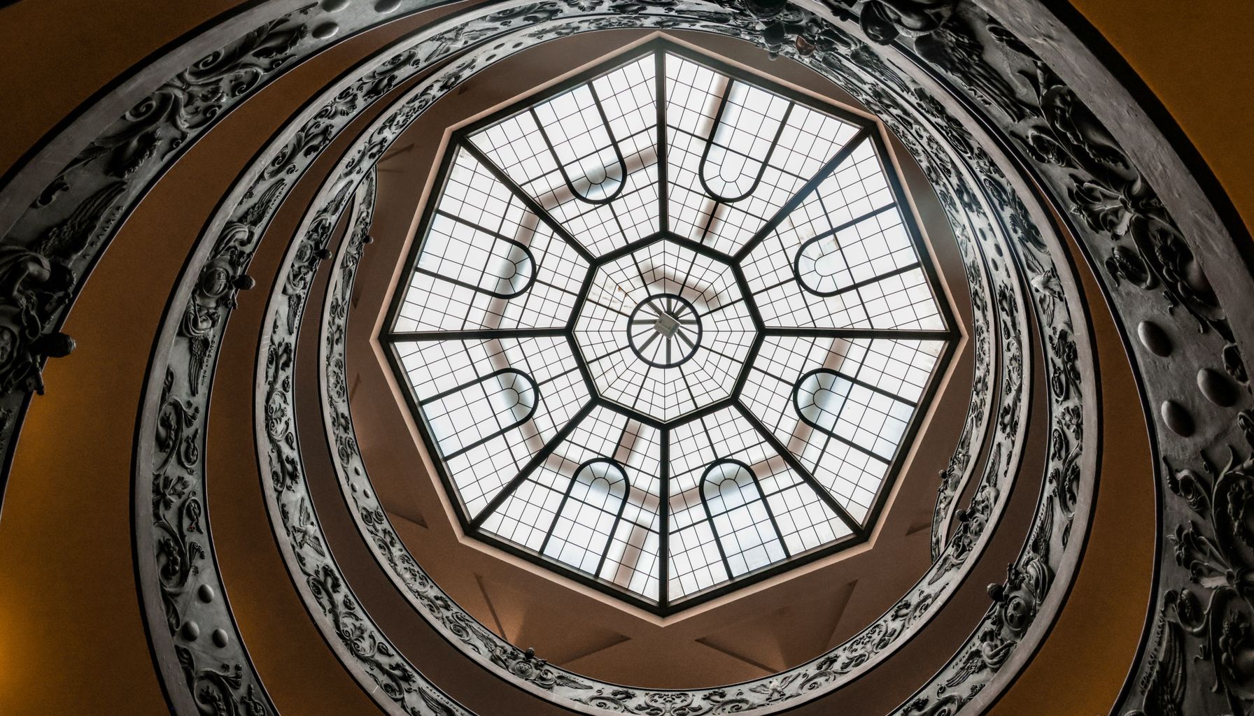 Intricate spiral staircase and elegant glass ceiling, showcasing Roman architectural beauty.