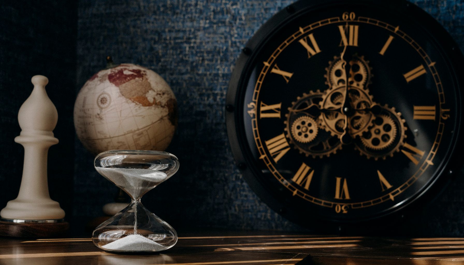 A dark and moody still life featuring an ornate clock, globe, and hourglass.