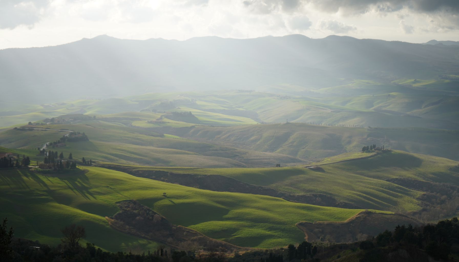 A breathtaking view of sunlit rolling hills in Tuscany, with dramatic skies and lush greenery.