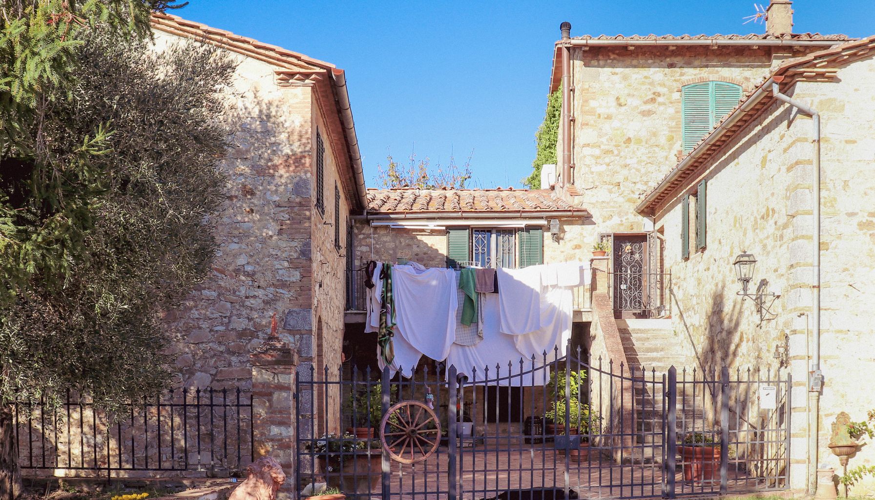 Stone house in Tuscany with laundry drying in the courtyard under a clear blue sky.