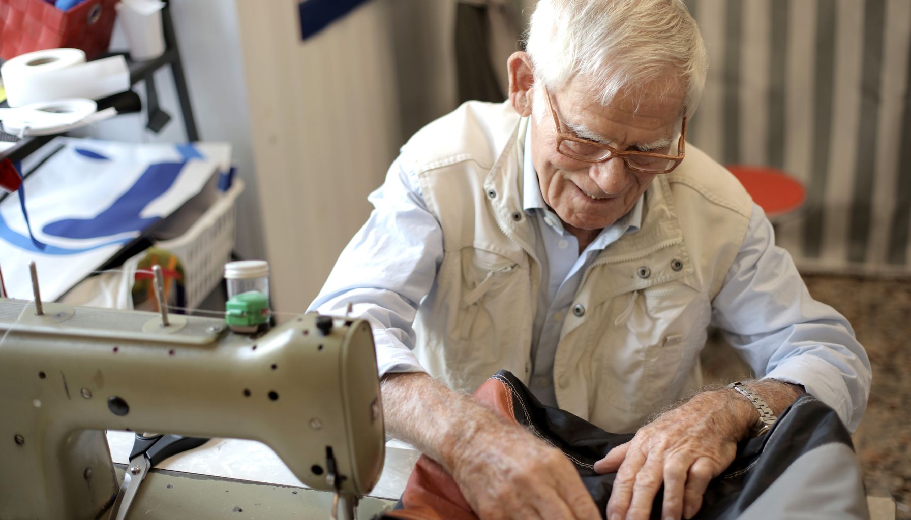 An elderly tailor skillfully working on a garment using a sewing machine in his workshop.