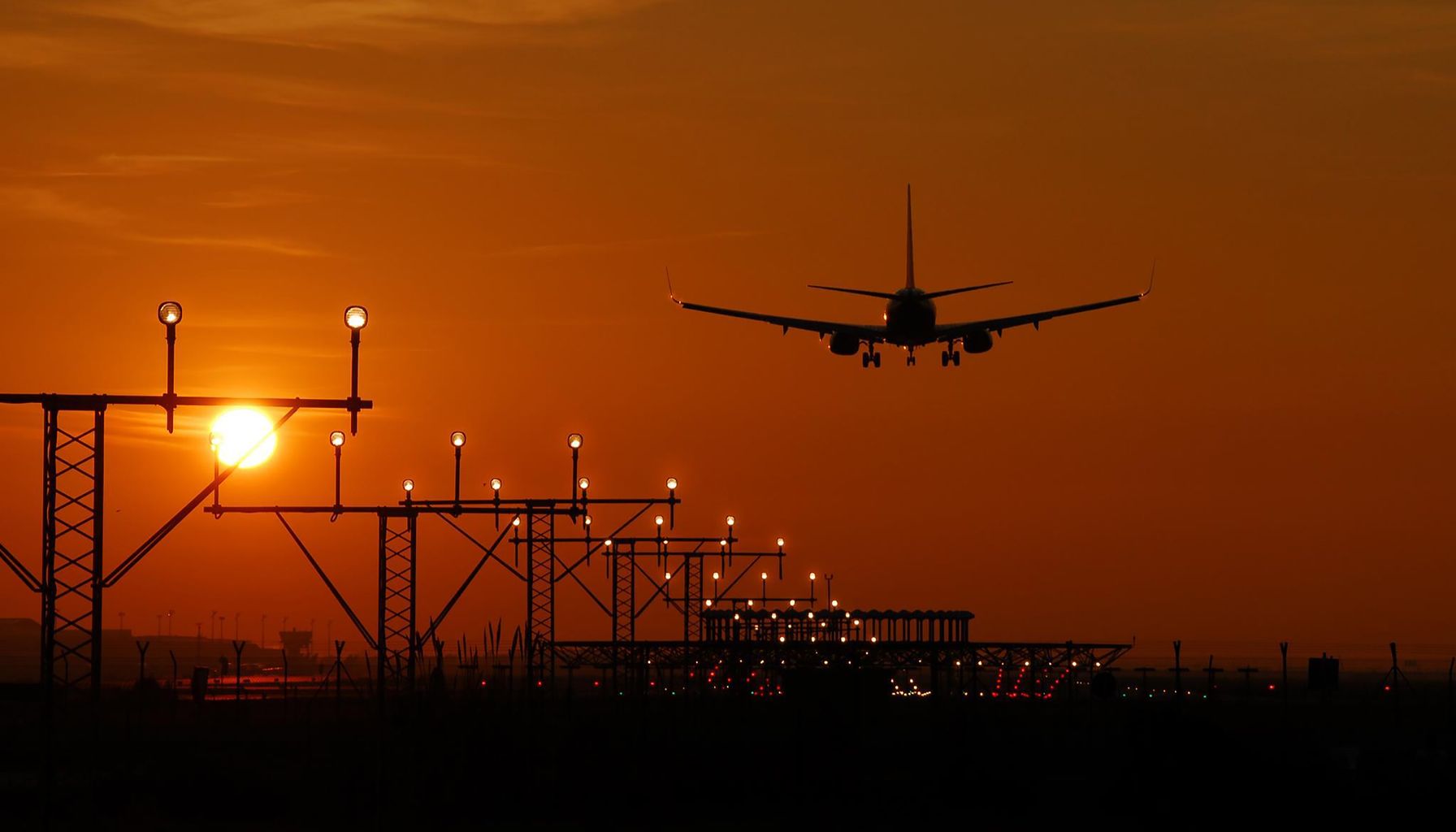 Silhouette of an airplane landing during sunset at Barcelona airport, with a vibrant orange sky.
