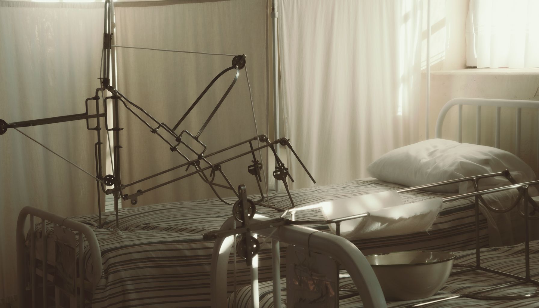 An empty hospital bed surrounded by medical equipment in a quiet, sunlit room.