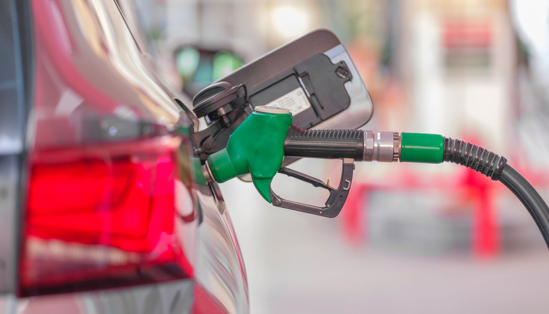 A close-up view of a fuel pump nozzle inserted into a car's tank at a gas station.