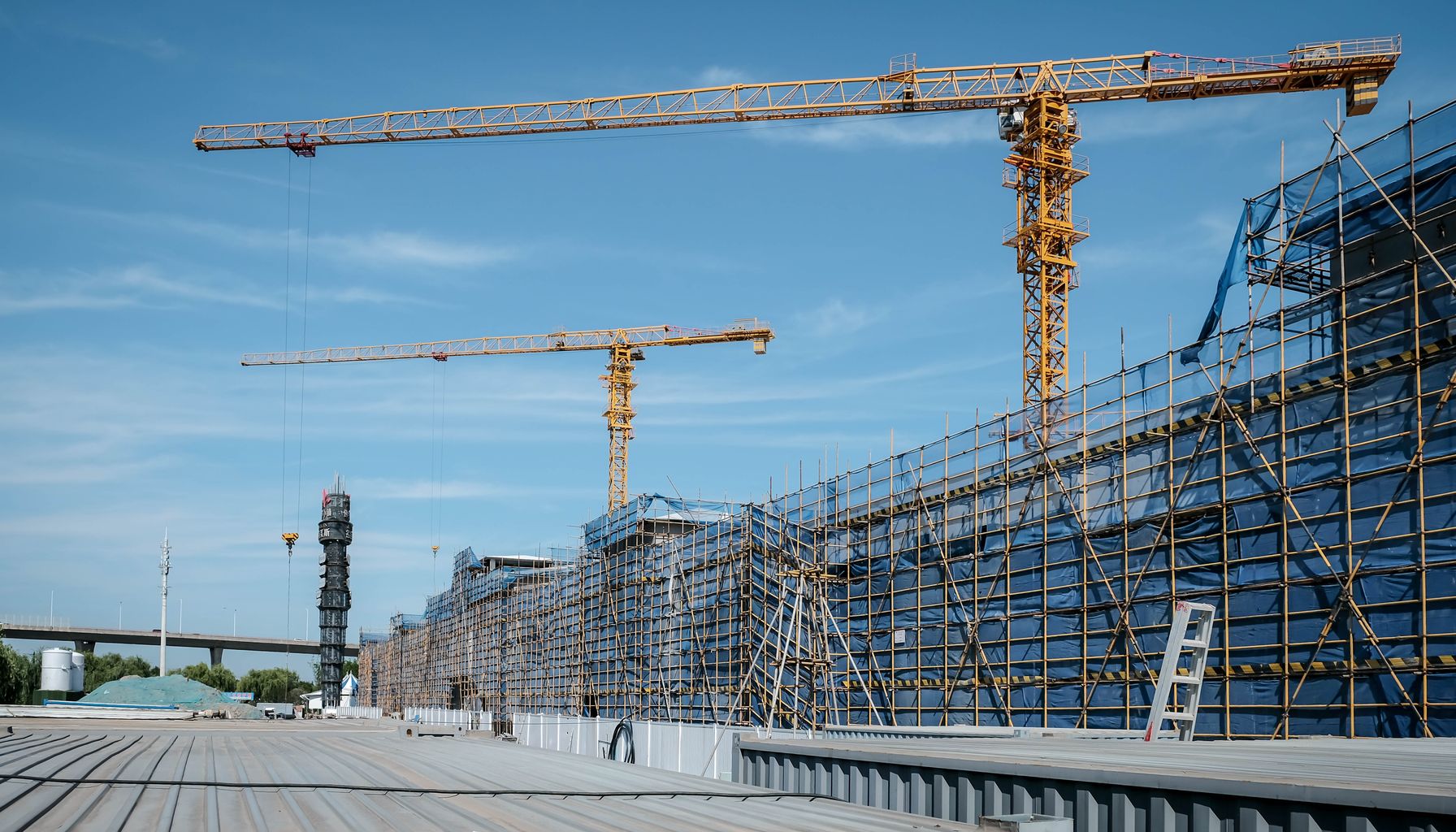 View of a construction site with yellow tower cranes and scaffolding under a clear blue sky.