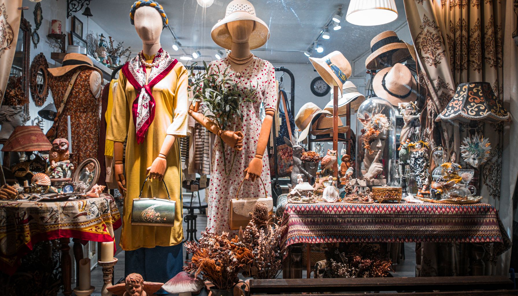 Charming vintage boutique window featuring dressed mannequins and ornate decor.