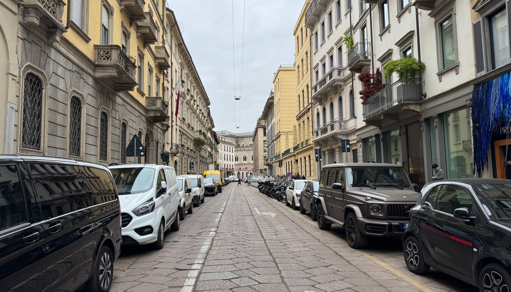 A picturesque street in Milan, Italy, showcasing classic European architecture and parked cars.