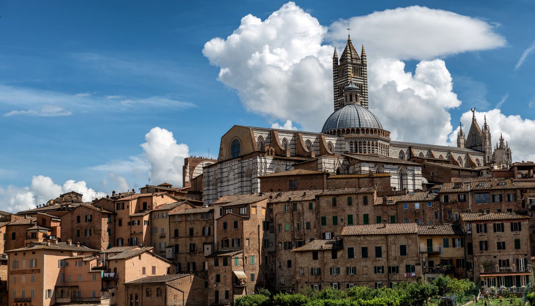The Siena Cathedral standing elegantly over the historic cityscape under a vibrant blue sky.