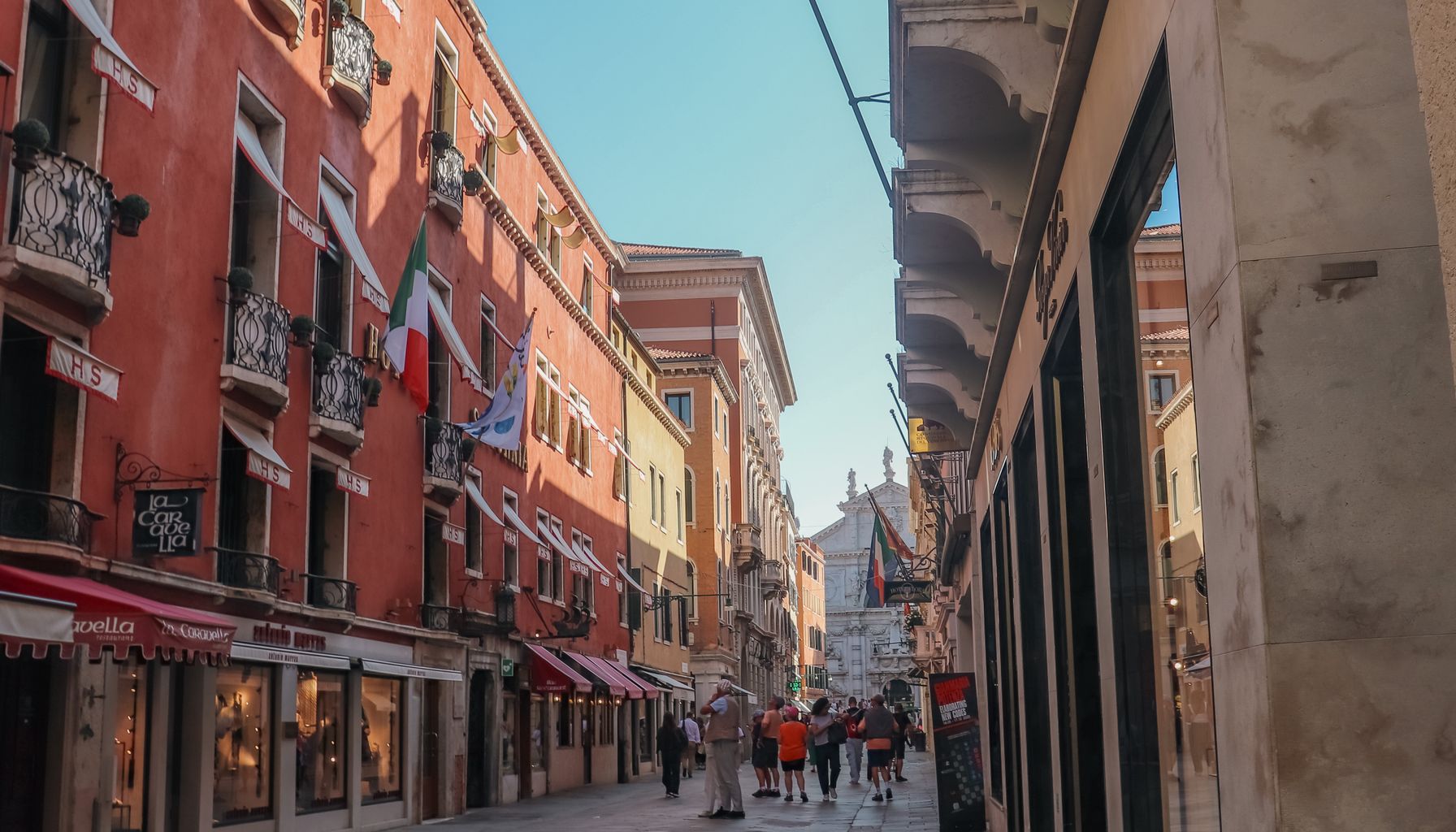 A vibrant street in Venice, Italy with Italian flags and tourists walking.